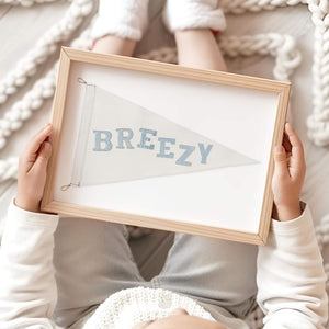 Child holding a framed 'Breezy' nautical flag in a cozy, knitted setting, emphasizing the light and airy aesthetic of seaside-inspired home decor.