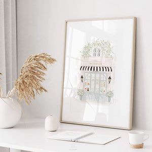 Stylishly framed Parisian patisserie watercolor print positioned on a home office desk, complemented by modern decor and natural light, evoking a serene workspace ambiance, by artist Leah Straatsma