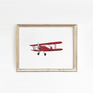 Elegantly framed art print of a vintage red biplane displayed on a white wall, complementing a bright and airy room with natural light flooding in, by artist Leah Straatsma